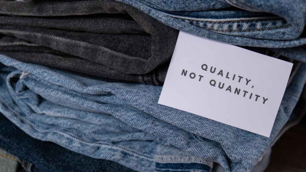 Sustainable Fashion Revolution message card reading Quality Not Quantity placed on folded denim garments