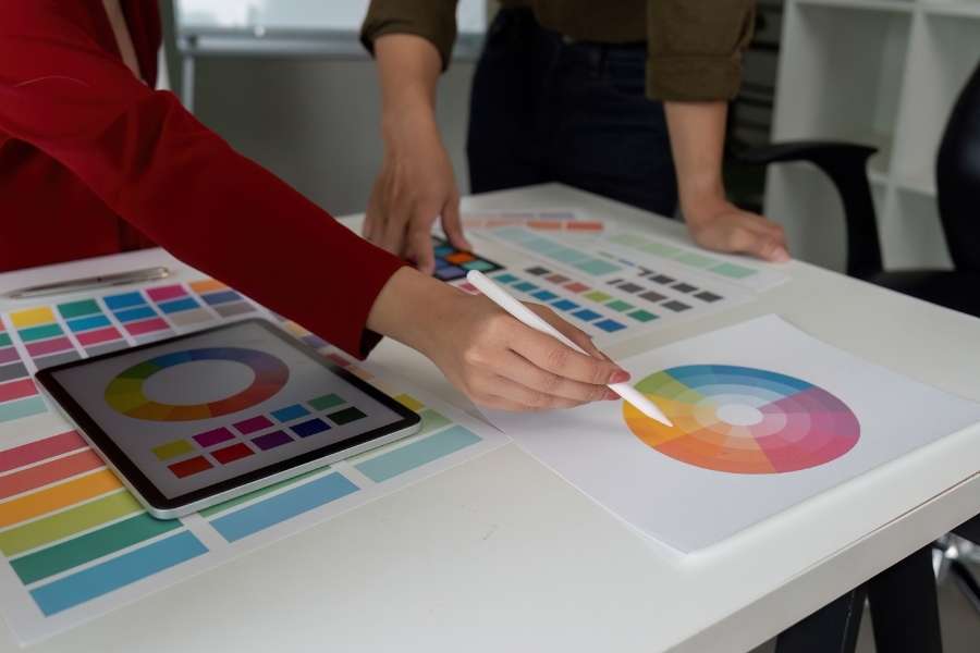 Designer analyzing color wheel and palette charts with tablet displaying digital color tools
