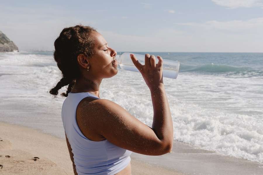 Woman drinking water on beach demonstrating mental health benefits of hydration and outdoor activities